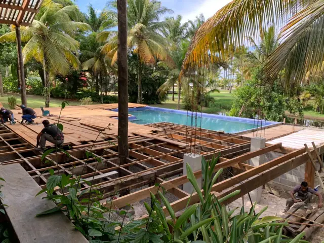 Estrutura nova do deck em vigas de madeira sobre brita, com pilares de concreto e piscina ao fundo, no Condomínio Txai