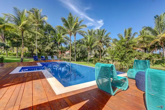 Deck de madeira e borda da piscina em pedra clara, com coqueiros ao fundo, em Itacaré