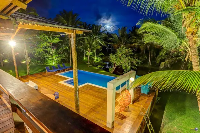 Vista do alto, à noite, do deck com pórtico, piscina e jardim iluminado